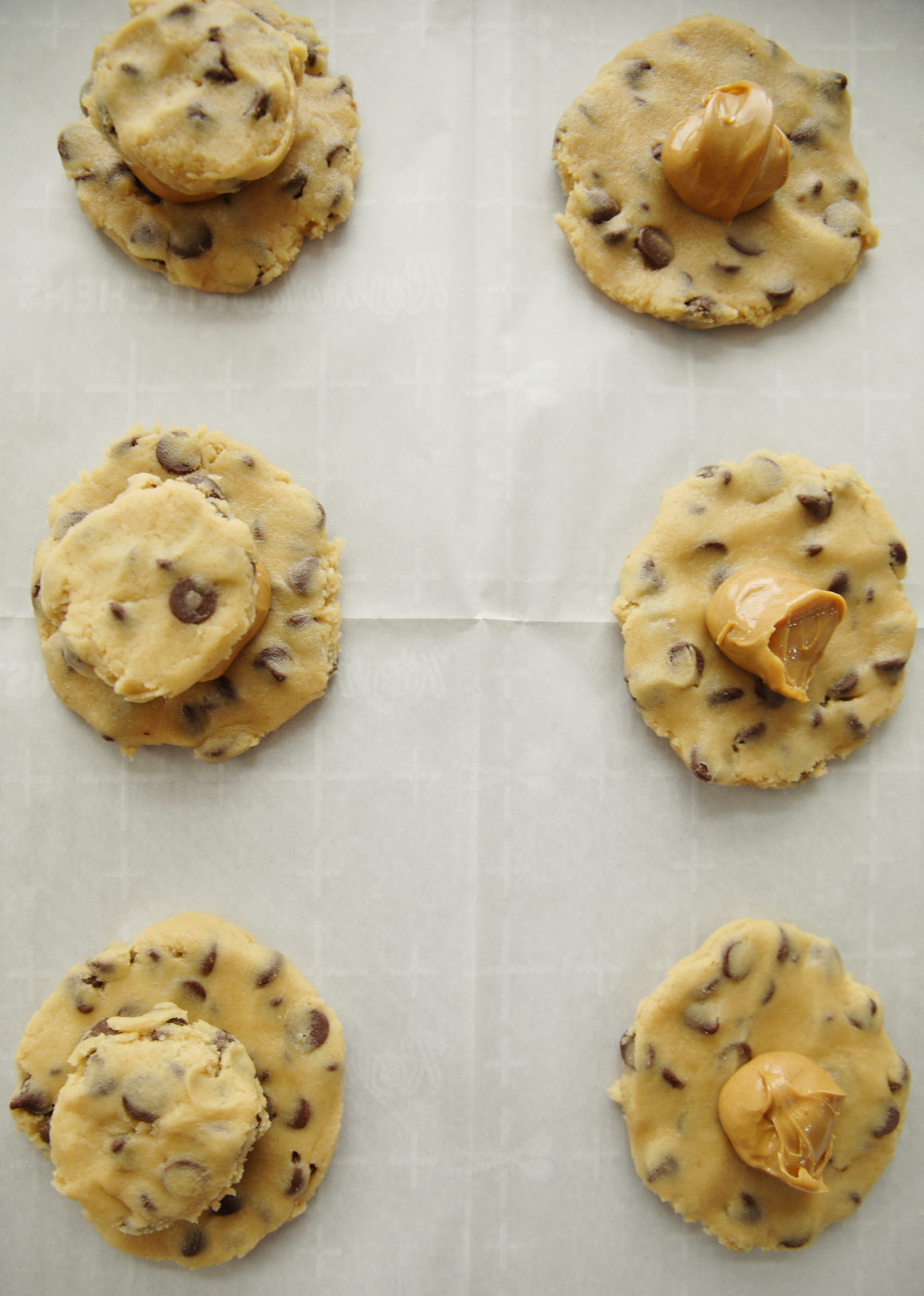 A process photo for peanut butter stuffed chocolate chip cookies.  You can see flat rounds of cookie dough laid out on parchment with mounds of peanut butter on all of them and a second small round of cookie dough on top of the peanut butter on some of the photos. 